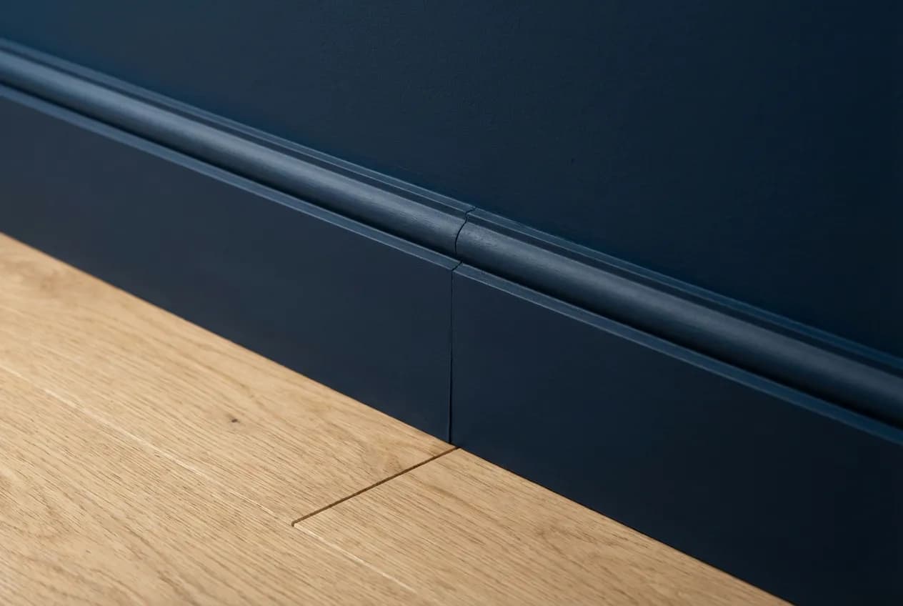 Faut-il peindre les plinthes comme le mur ? Le Guide Déco Gros plan sur une plinthe bleu marine peinte de la même couleur que le mur sur parquet