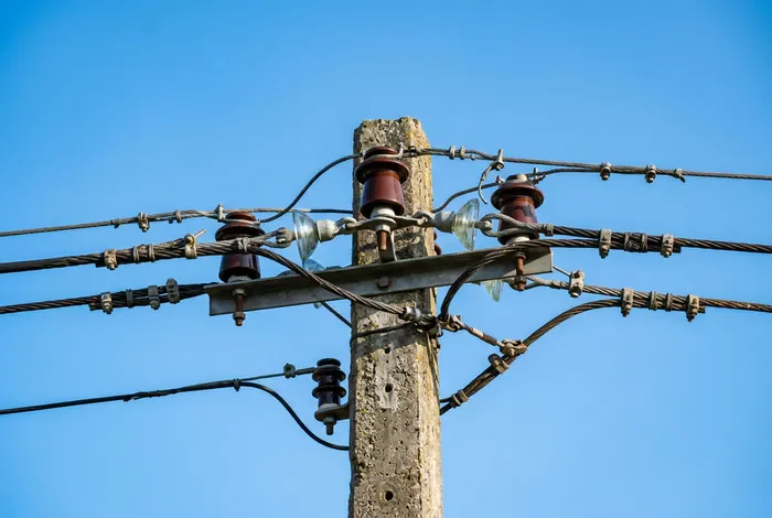 Tarif pour déplacer un poteau EDF : Prix 2026 - Déplacer un poteau EDF : Le guide du vrai tarif ! - Poteau EDF gênant : Quel tarif et qui doit payer ? Câbles électriques et raccordements en haut d'un poteau sur fond de ciel bleu.